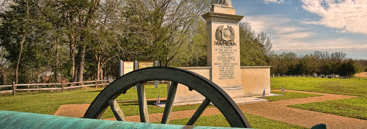 Photograph of a cannon in the foreground and a monument in the background on a battlefield.