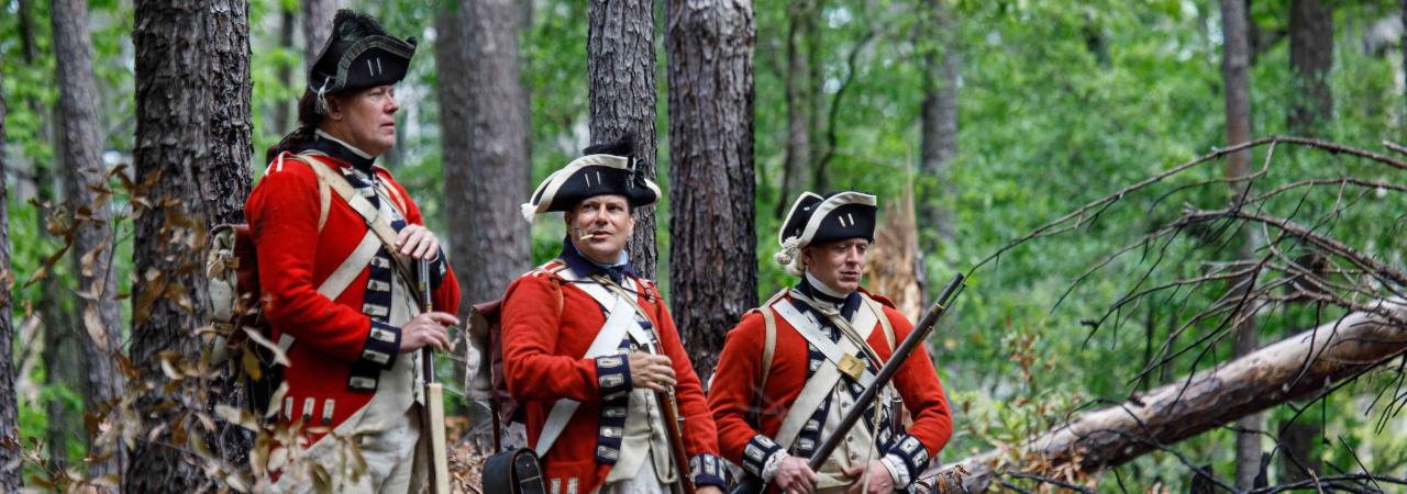 Three British soldiers dressed in uniforms from the American Revolution in a forest. 