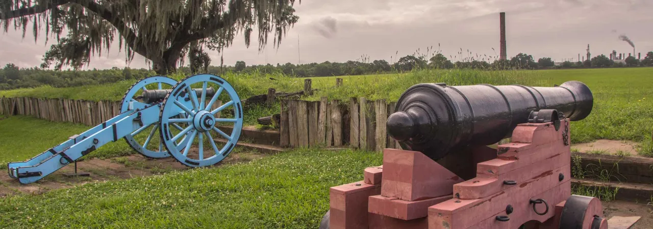 Two cannons stand upon Chalmette Battlefield, La. surrounded by urbanization.