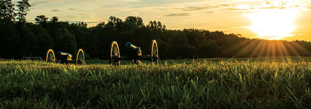 Two cannons sit side-by-side with a radiant sunrise in the background at Chancellorsville Battlefield