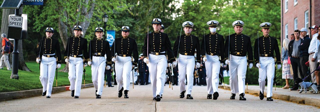 cadets in uniform march in line down a street