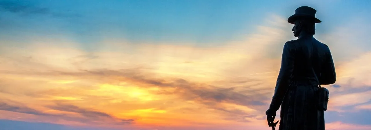 A statue stands at Little Round Top against a vibrant sunset.