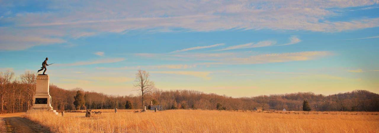 Monument at the edge of an autumnal field with clouds across a blue sky