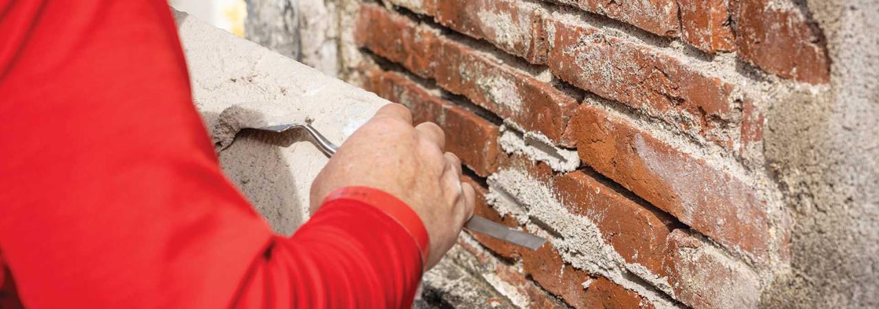 An individual's arm is seen applying mortar to a brick wall.