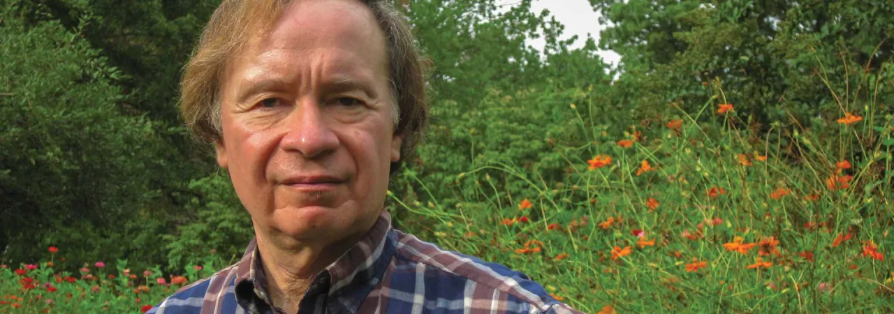 A photograph of a man standing in front of trees and wildflowers on a battlefield