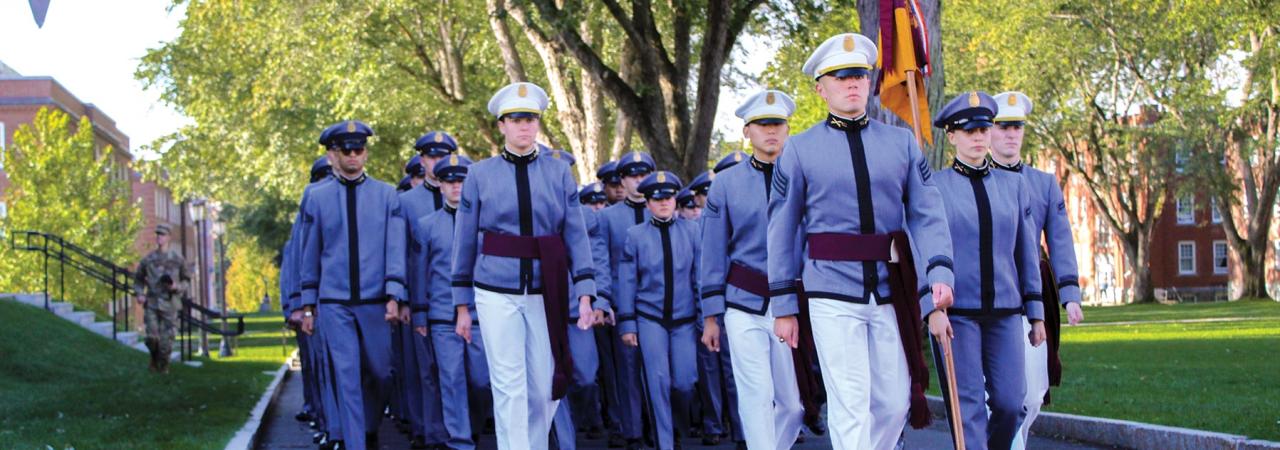 Cadets in grey and white uniforms marching on a school campus