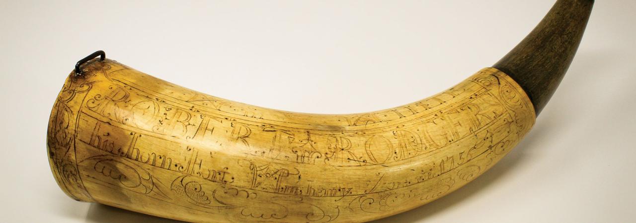 Photo of a powder horn with detailed engravings shown on a plain background.