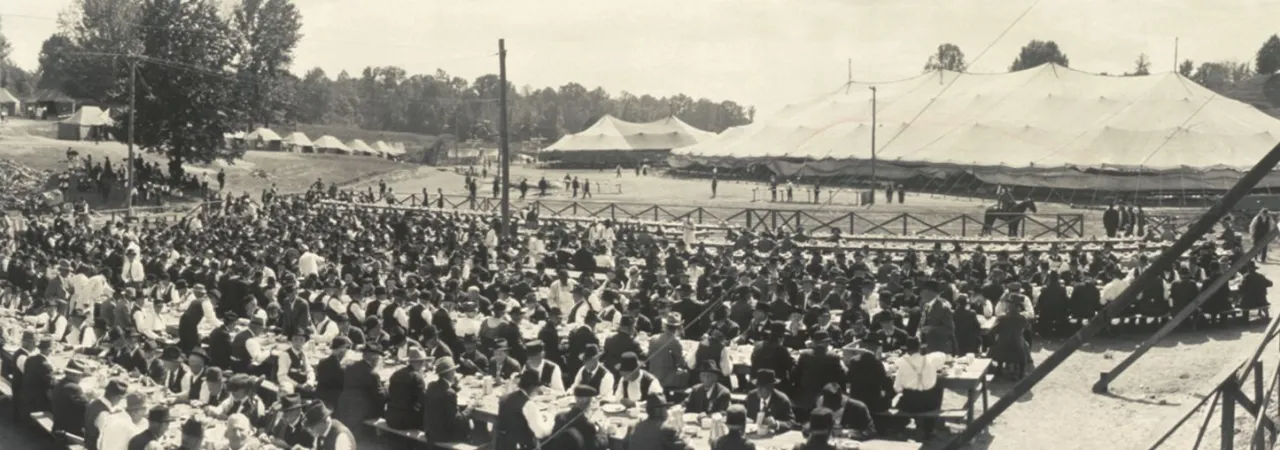 Black and white photograph of an outdoor mess hall with rows of men seated at long tables