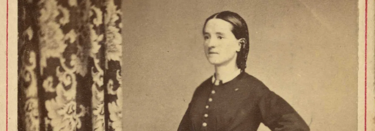 Full-length studio portrait of Civil War surgeon Mary Edwards Walker standing in profile with one hand resting on a book.