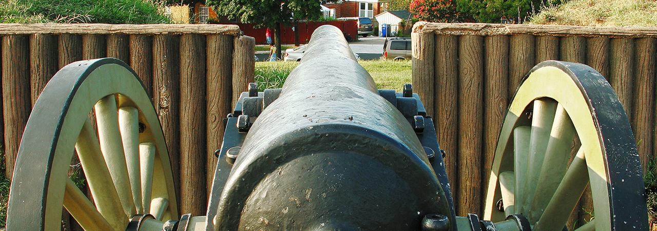 Rear view of a cannon near a wooden fence. 