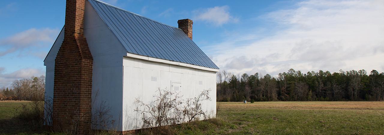 Photograph of a white brick building in the foreground with a battlefield in the background. 