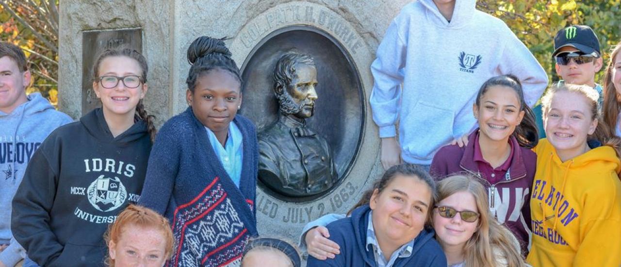 Students post with their teacher in front of a marker at Gettysburg.