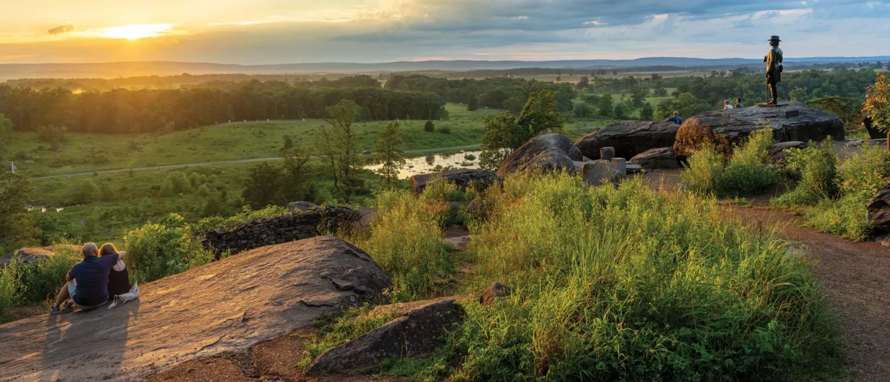A couple sits on the rocks at Little Round Top at sunset