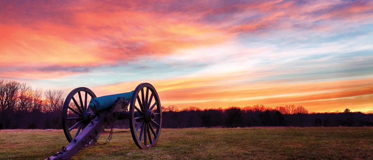 A cannon at Manassas National Battlefield Park under a vivid orange-purple sky.