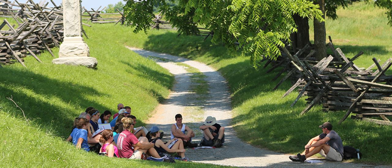 This photograph depicts a group of people sitting in a circle on the grounds of Antietam.