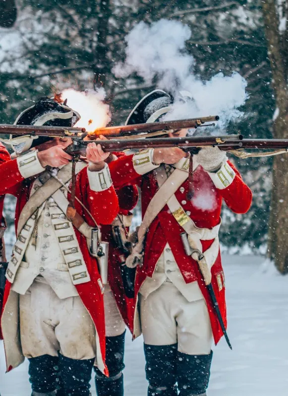 Three men standing together dressed in colonial soldiers' uniforms firing muskets