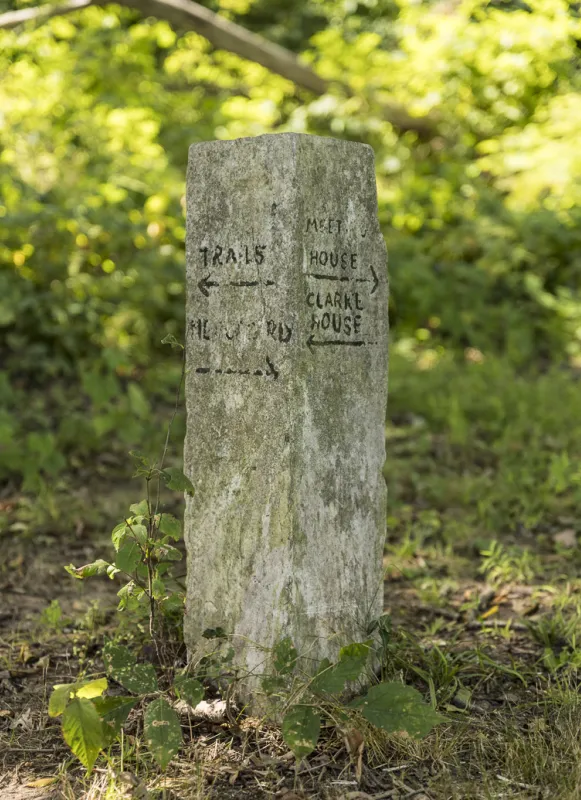 Weathered stone trail marker at Princeton Battlefield State Park with hand-painted arrows pointing toward nearby trails, the Mercer House and Clarke House.