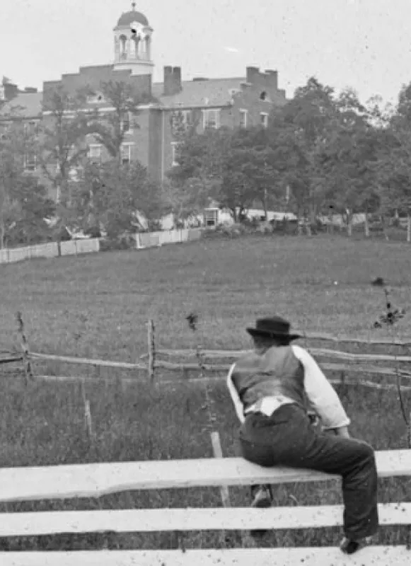A man straddles a fence in the foreground of this 1864 photograph of the Lutheran Theological Seminary in Gettysburg, Pennsylvania.
