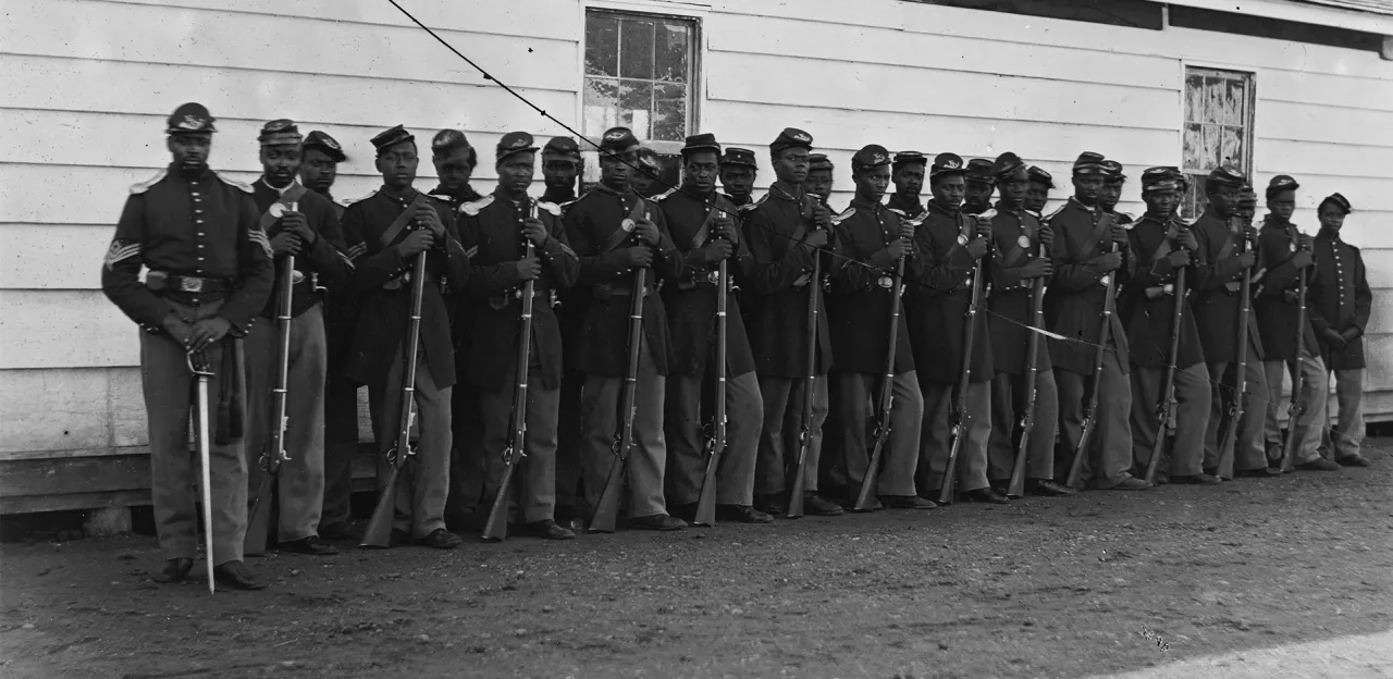 Photograph of Washington, 1862-1865, view of the defenses of Washington. Shows 27 African Americans in two lines with rifles resting on the ground.
