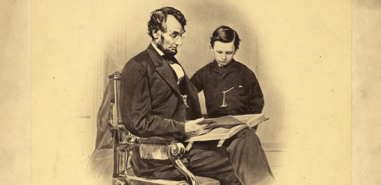 President Abraham Lincoln sits wearing spectacles beside his young son Tad, examining a book altered in the photograph to resemble a Bible.