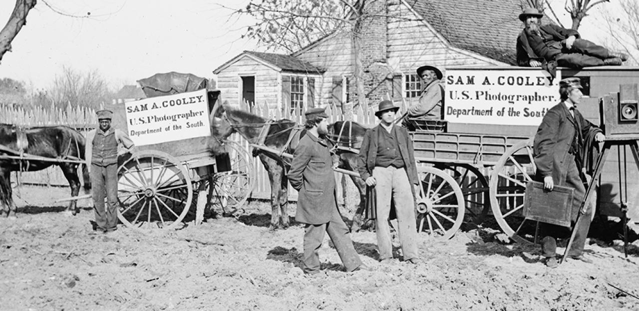 A black and white photograph of men advertising with signs posted on their horse and buggies