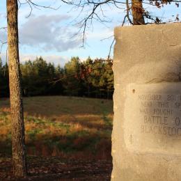 Photograph of a battlefield with a stone marker in the foreground. 