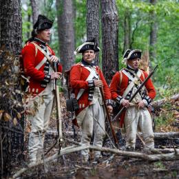Three British soldiers dressed in uniforms from the American Revolution in a forest. 
