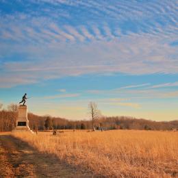 Monument at the edge of an autumnal field with clouds across a blue sky