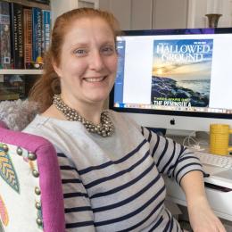 Portrait of Mary Koik with the cover of an issue Hallowed Ground on her monitor screen