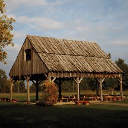 Wooden. shelter with picnic table and benches beneath it at a park setting