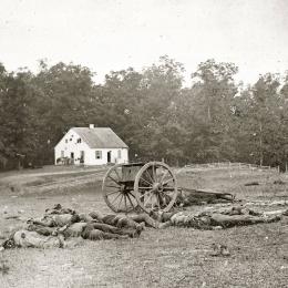 A black and white photograph of Dunker Church with Confederate Dead and a cannon in the foreground.