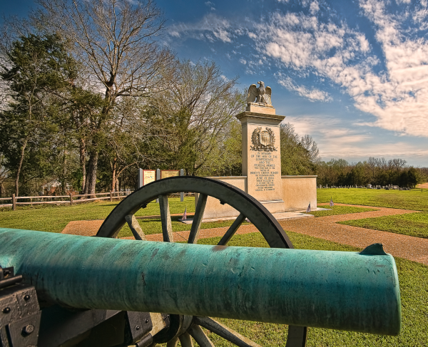 Photograph of a cannon in the foreground and a monument in the background on a battlefield.