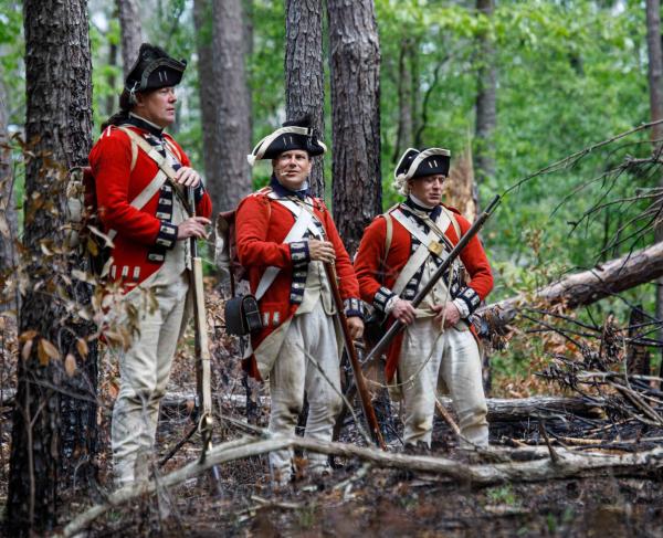 Three British soldiers dressed in uniforms from the American Revolution in a forest. 