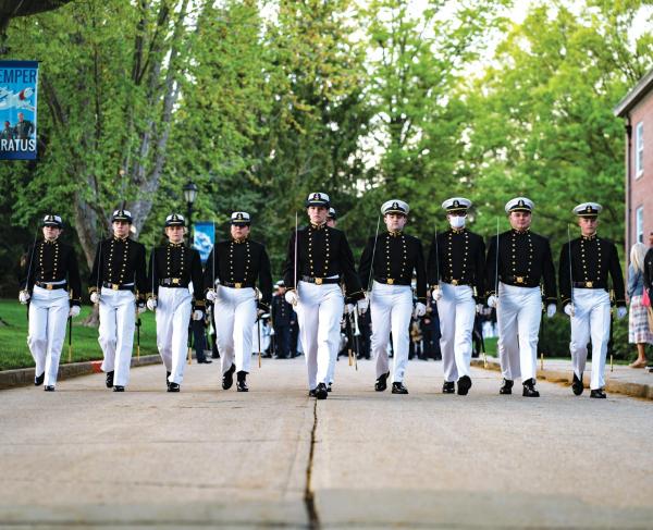 cadets in uniform march in line down a street