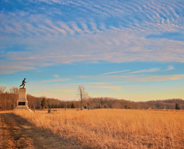 Monument at the edge of an autumnal field with clouds across a blue sky