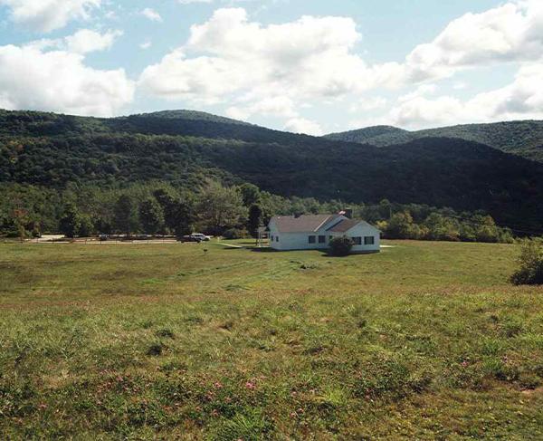 Photograph of a grassy battlefield with a white house in the mid-ground and a mountain range in the background.