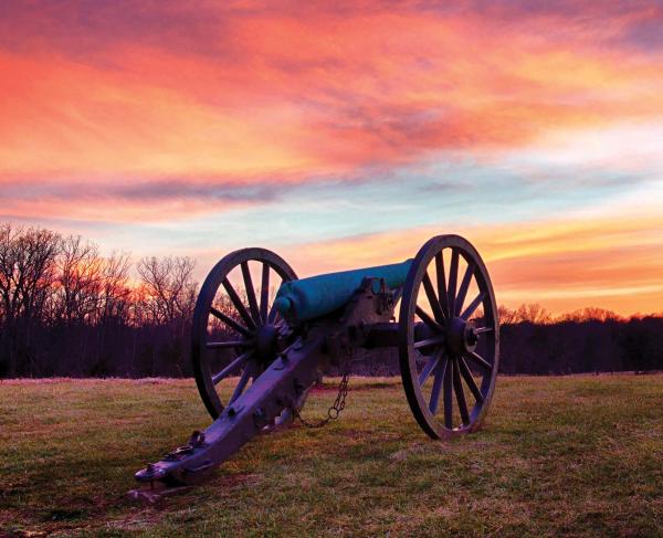 A cannon at Manassas National Battlefield Park under a vivid orange-purple sky.