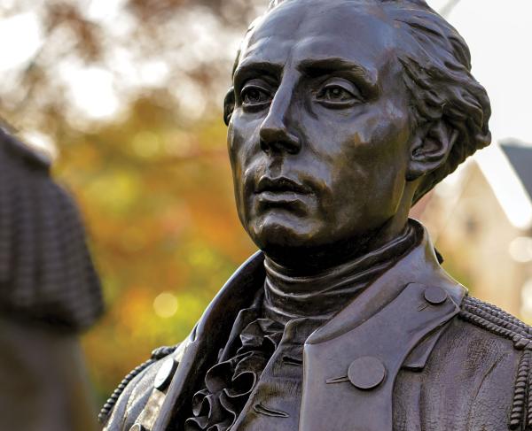 Bust of bronze statue of Revolutionary War era gentleman with foliage in the background