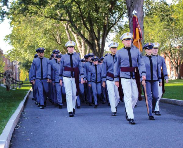 Cadets in grey and white uniforms marching on a school campus