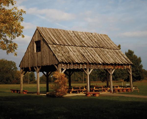 Wooden. shelter with picnic table and benches beneath it at a park setting 