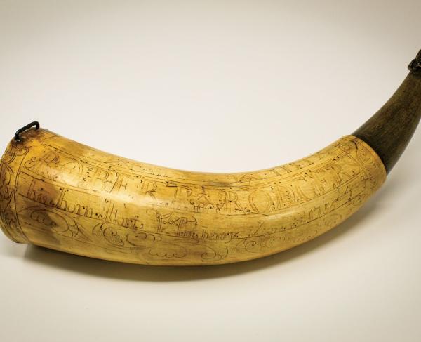 Photo of a powder horn with detailed engravings shown on a plain background.