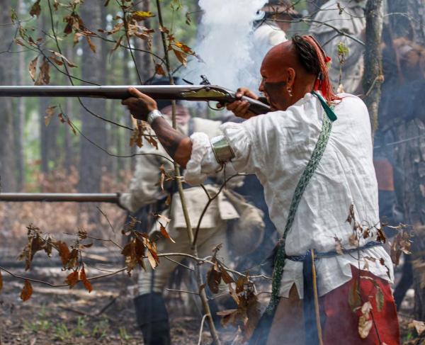 A Catawba reenactor aiming a rifle