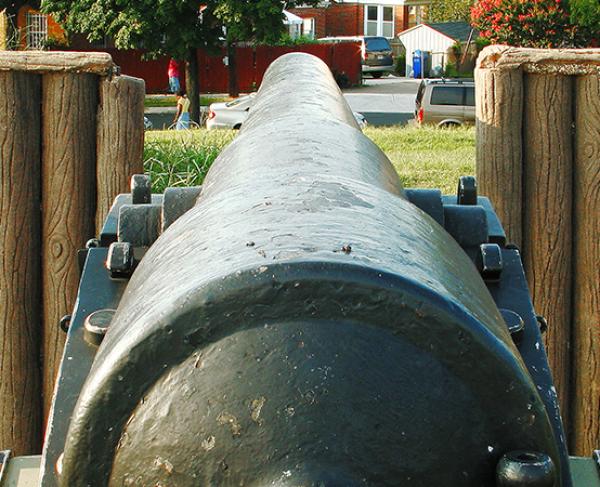 Rear view of a cannon near a wooden fence. 