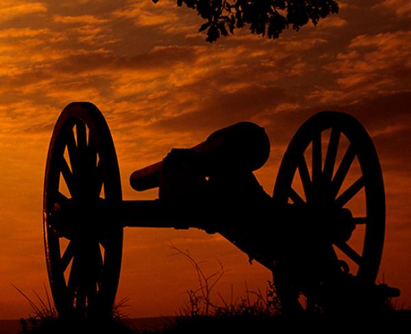This photo depicts a silhouette of a canon amidst a vibrant, orange sunset. 