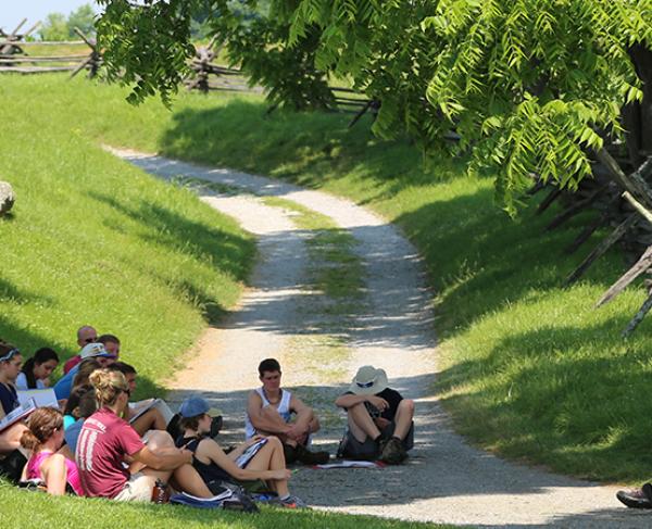 This photograph depicts a group of people sitting in a circle on the grounds of Antietam. 