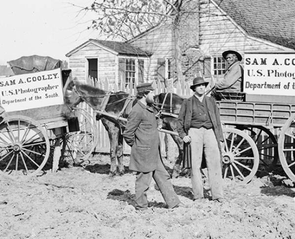 A black and white photograph of men advertising with signs posted on their horse and buggies