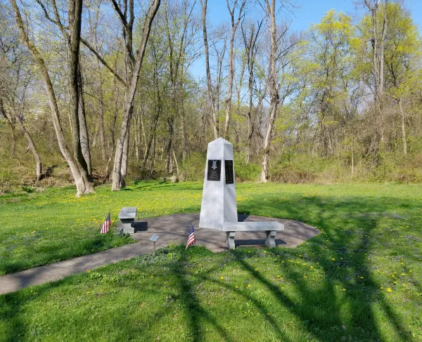 Obelisk with stone benches surrounded by woodland. 
