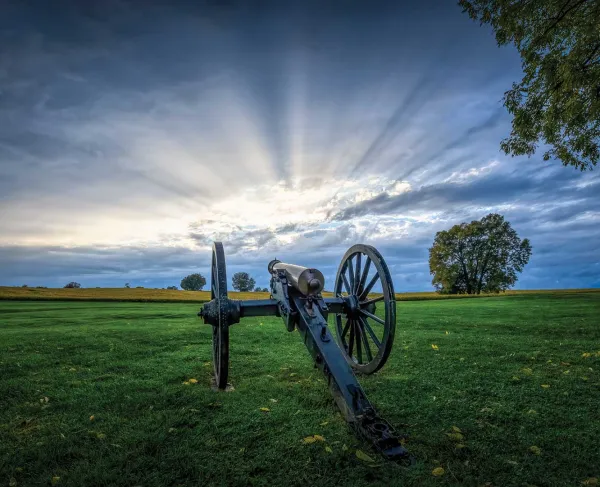 A cannon sits on Antietam National Battlefield, rays of sunlight beam from the sky.