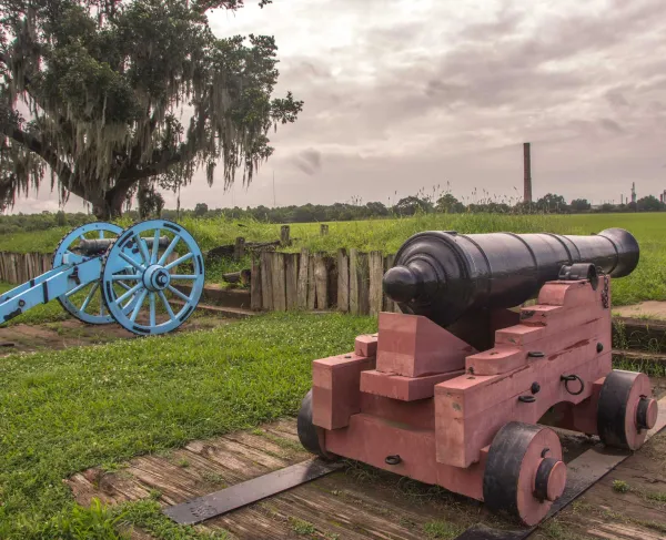 Two cannons stand upon Chalmette Battlefield, La. surrounded by urbanization.