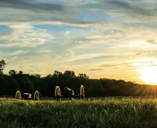Two cannons sit side-by-side with a radiant sunrise in the background at Chancellorsville Battlefield